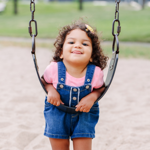 toddler in overalls leaning on a swing