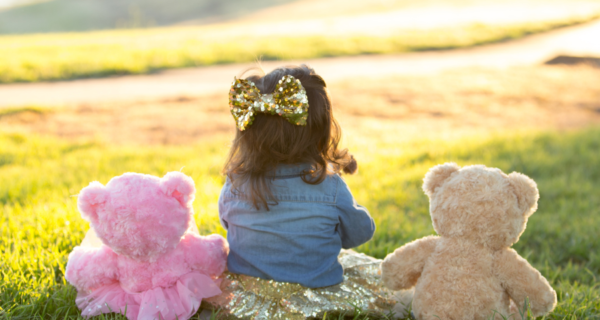 Child In A Bow Sitting In Between Two Teddy Bears