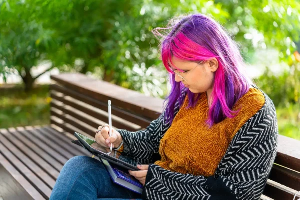 tennyson-center-TREE A young woman with autism draws on a tablet while sitting on a bench